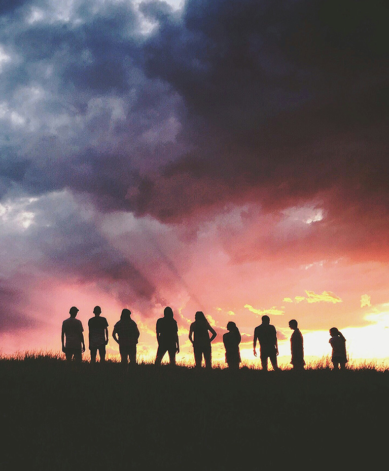 Menschen als Silhouetten auf einem Hügel bei Sonnenuntergang als Symbol für Partnerschaft und Zusammenarbeit